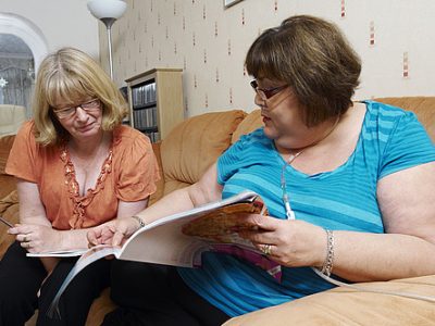 Two women sitting on a sofa, one wearing a oxygen supply tube.