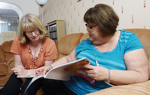 Two women sitting on a sofa, one wearing a oxygen supply tube.