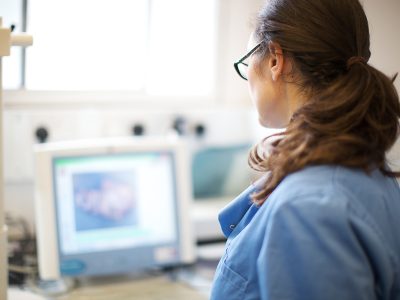 A woman in a blue uniform, looking at a computer screen in a laboratory