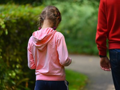A young girl with her back to the camera and her hair in plaits, wearing a pink hoodie in a park