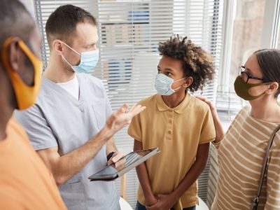 A doctor talks to a family including a teenage boy, all wearing masks