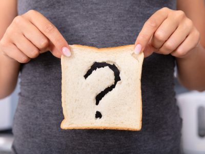 A woman holds a slice of bread with a question mark cut out of it
