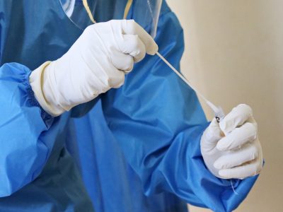person in gown and latex gloves puts swab in sample tube.