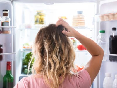 A woman scratches her head in confusion while looking in a fridge
