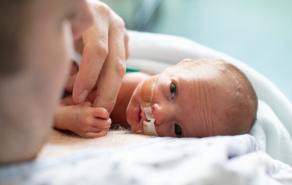 A father holds hands with his premature baby in hospital