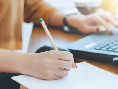 A woman is taking notes while working on her laptop