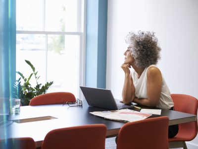 A woman looks reflectively out of a window while sitting at a computer