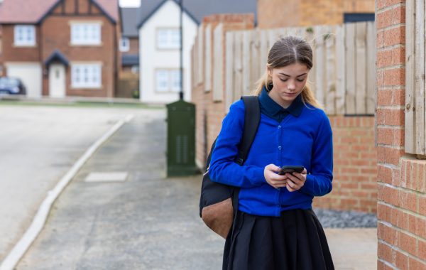 A young person walks home from school while looking at their mobile phone