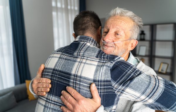 An older man with an oxygen tube embraces a younger man