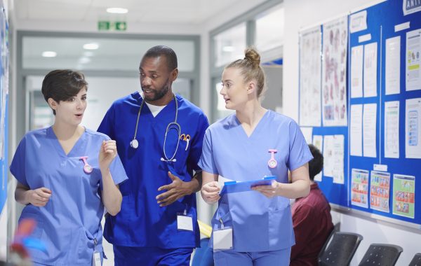 Three healthcare professionals talking in a hospital corridor