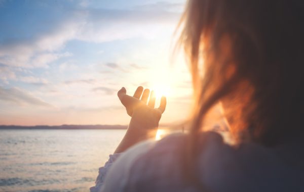 A woman at sunrise over the sea, cupping the sun in her hands