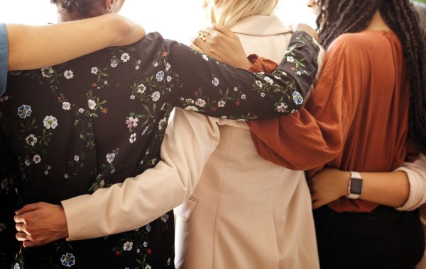 Close-up of a group of women, seen from the back, with their arms around each other